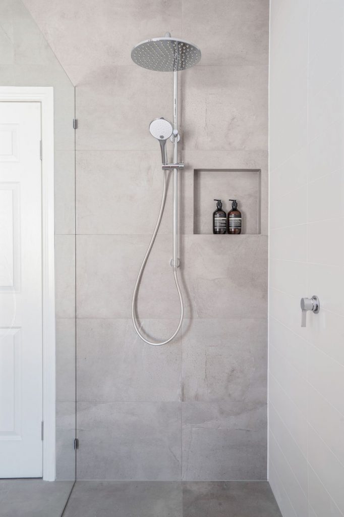 big shower head in shower with grey tiles, nook and detachable shower head